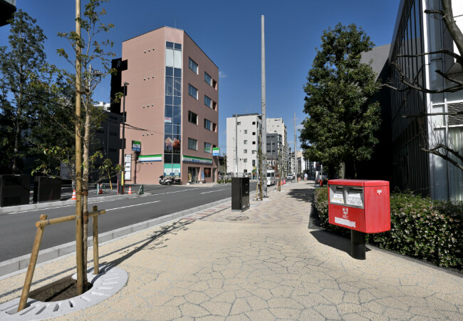 赤い郵便ポストがある歩道を直進します。道の向かい側にはファミリーマートがあります。