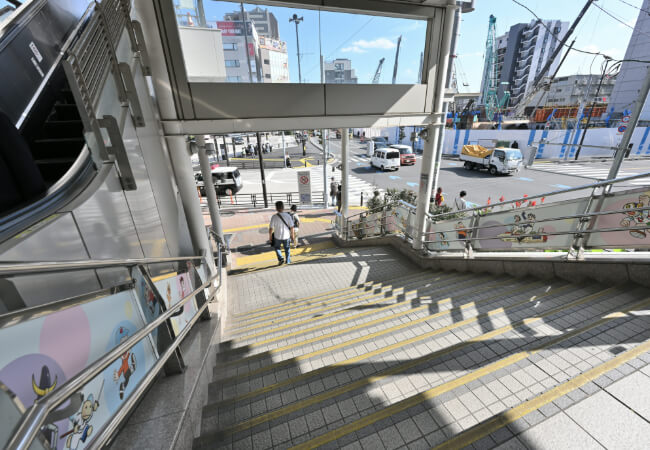 キャラクターのイラストがある階段駅前の通りへ出る